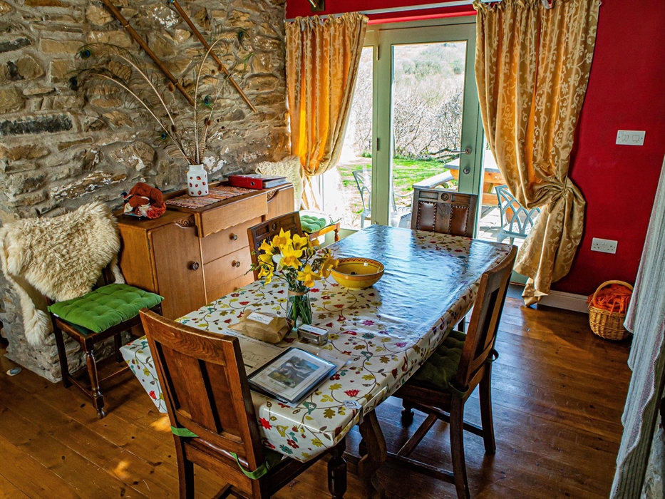 Cwt Mochyn cottage dining room with wood floor, red walls and French window leading out onto the patio