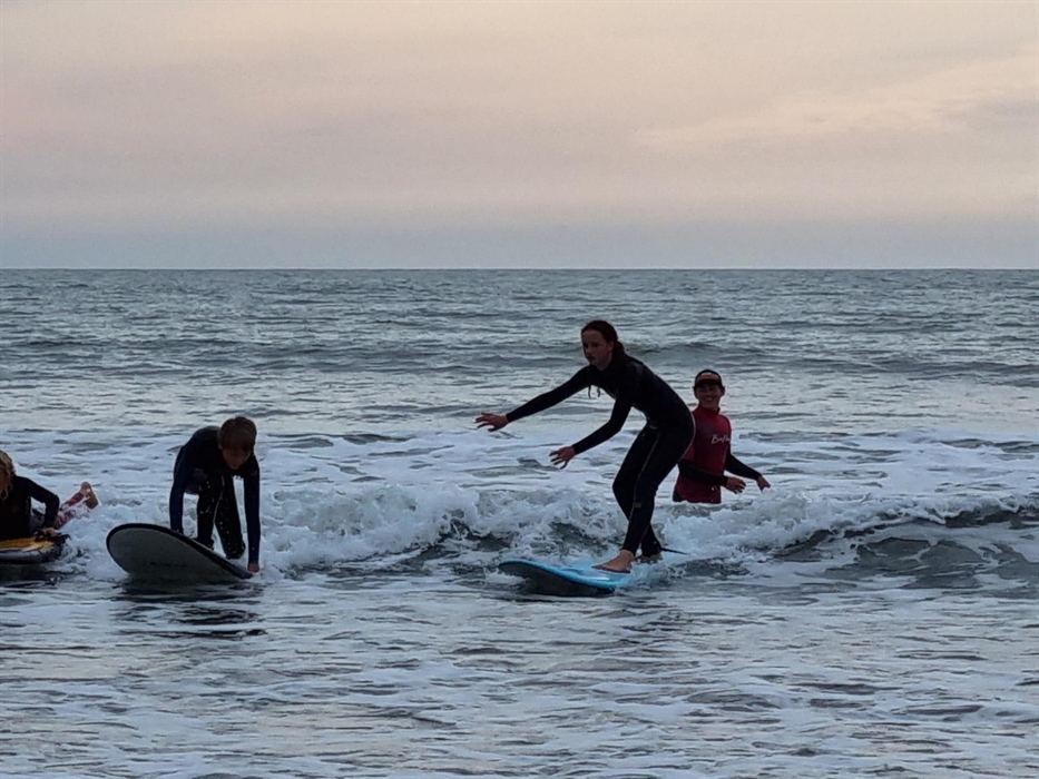 3 surfers ctaching the same wave, while the surf coach looks on.