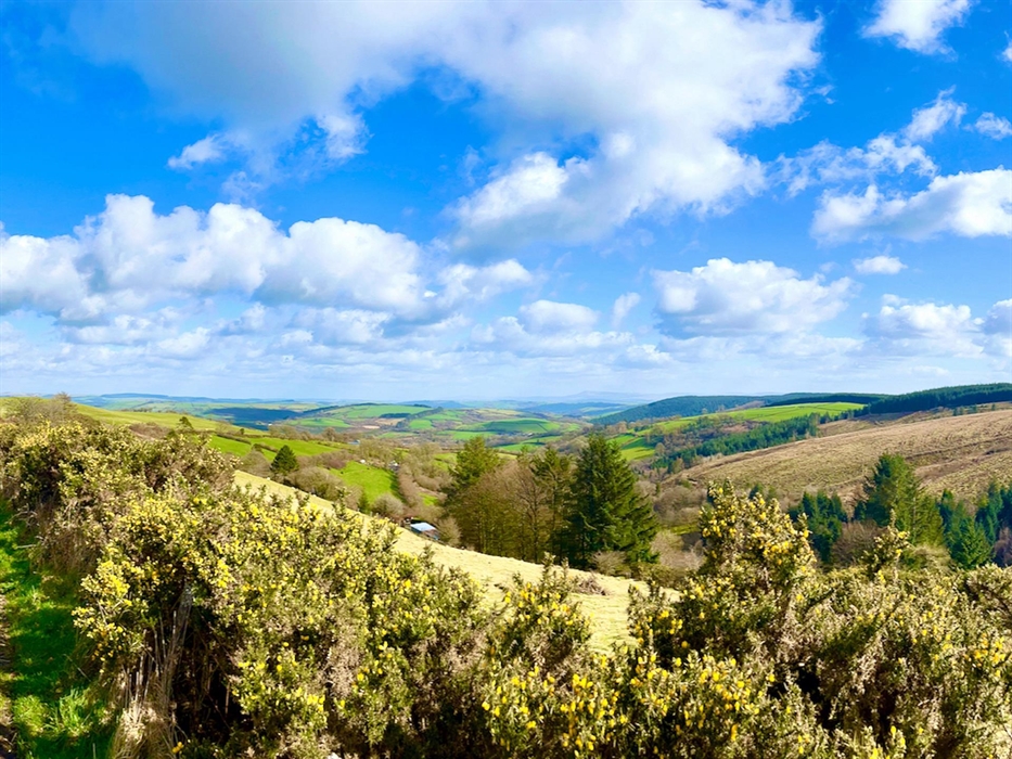 A view over the surrounding countryside with blue skies, a patchwork of fields and the Brecon Beacons in the distance