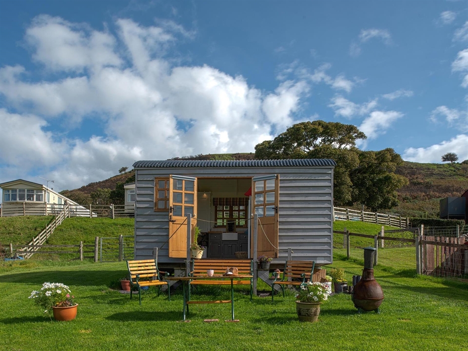 This shows the hut with the double doors open so you can see the kitchen with a Belfast sink.  and the outside seating area.  There is a table, bench