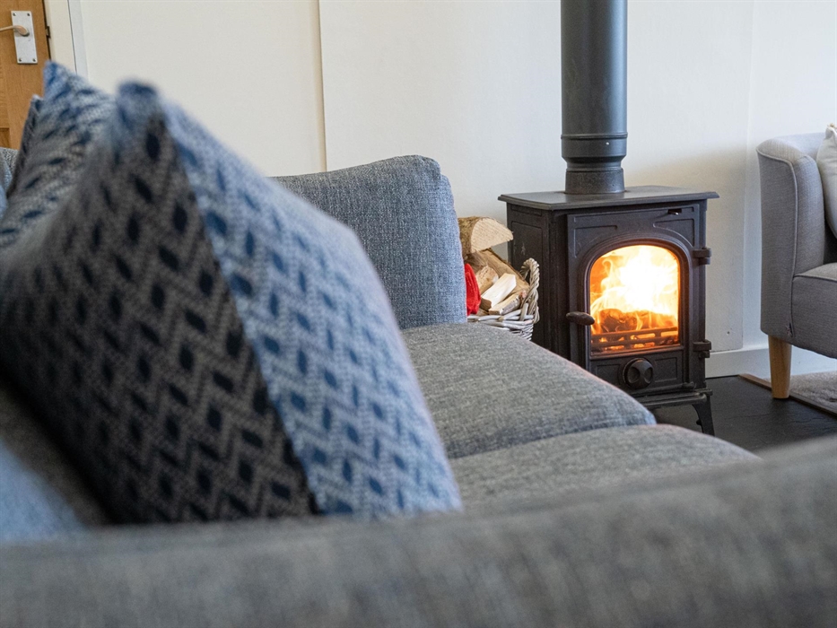 Comfy sofa and puffy cushions in the open plan living room with roaring log burner on slate hearth.