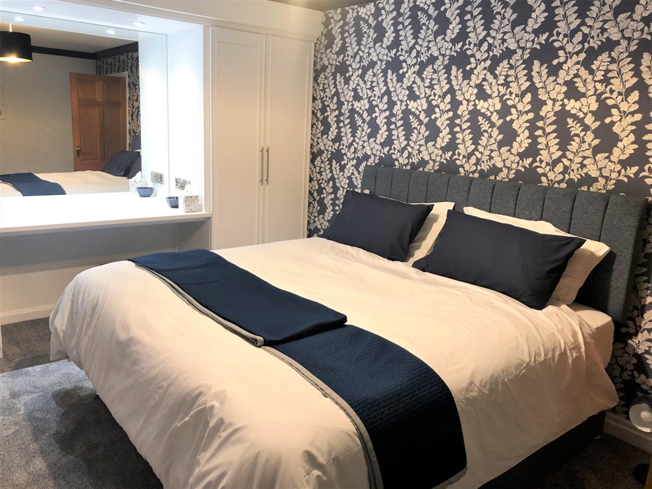 Bedroom with large dressing table and king size bed with blue wallpaper and throw on the bed