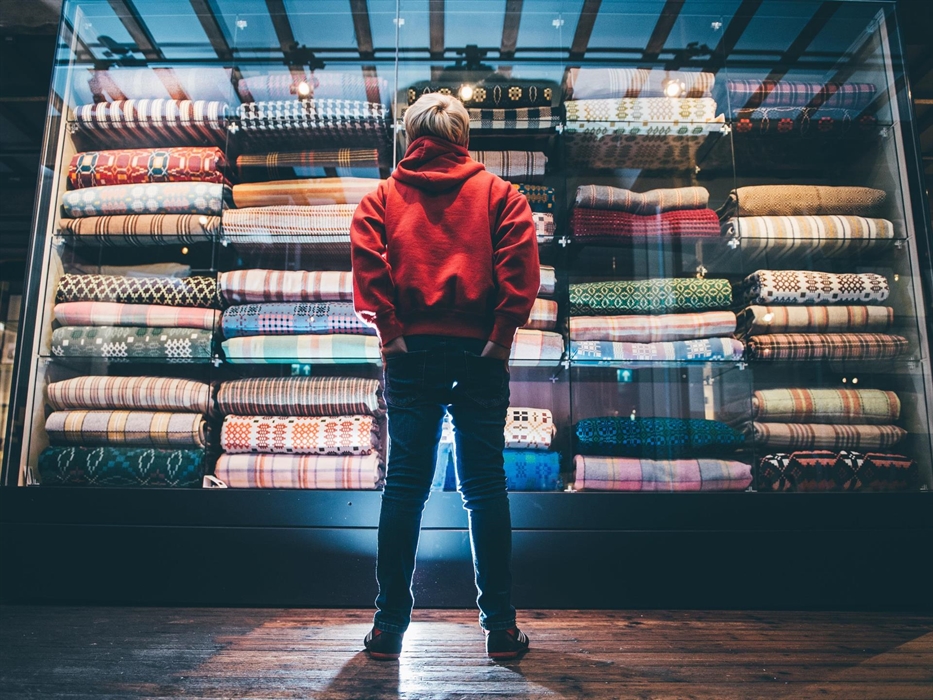 a boy in a red hoodie and jeans stands with his back to us. He is looking at a huge glass display case than goes from the floor to the ceiling. the ca