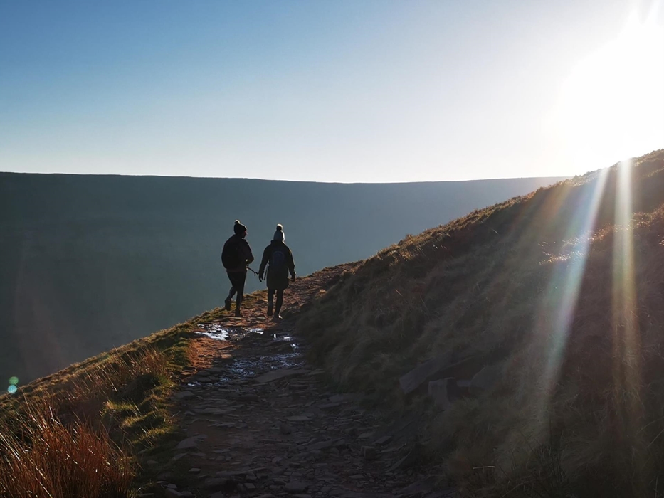 Two walkers heading along a rough stony path into the sunlight