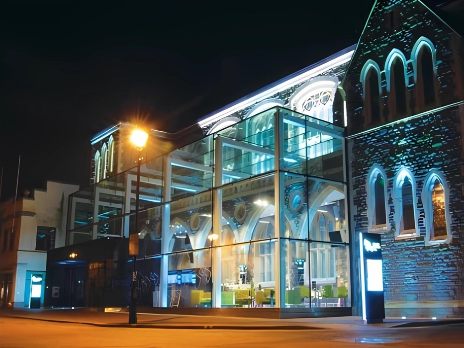 External street view at night time image of the Gwyn Hall. Highlighting the cafe area in the glass atrium