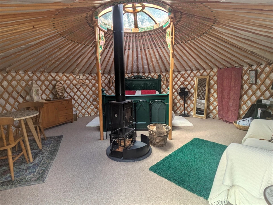 The yurt is round with many painted wood rafters radiating from the central roof light. There is a central logburner on a round slate hearth. At the b