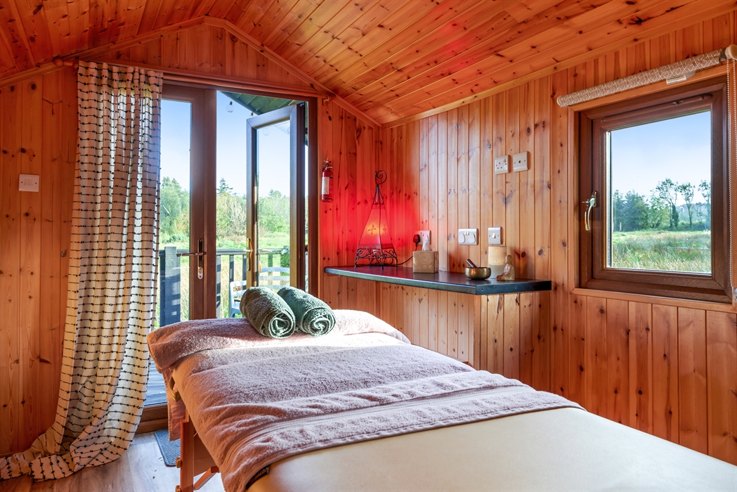 Holistic therapy cabin with a massage table and a view of the meadow in the background