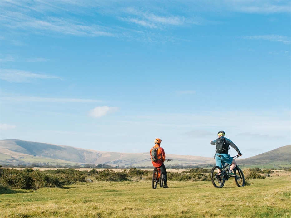 Two mountain bikers look across the Preseli Hills on a sunny day with blue skies.