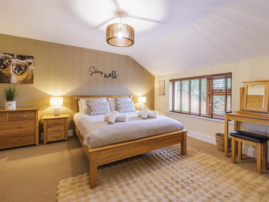 Sheep wall canvas above wooden chest of drawers, side tables with lamps either side of a king size bed with sheep cushions and a "Sheep Well" sign on