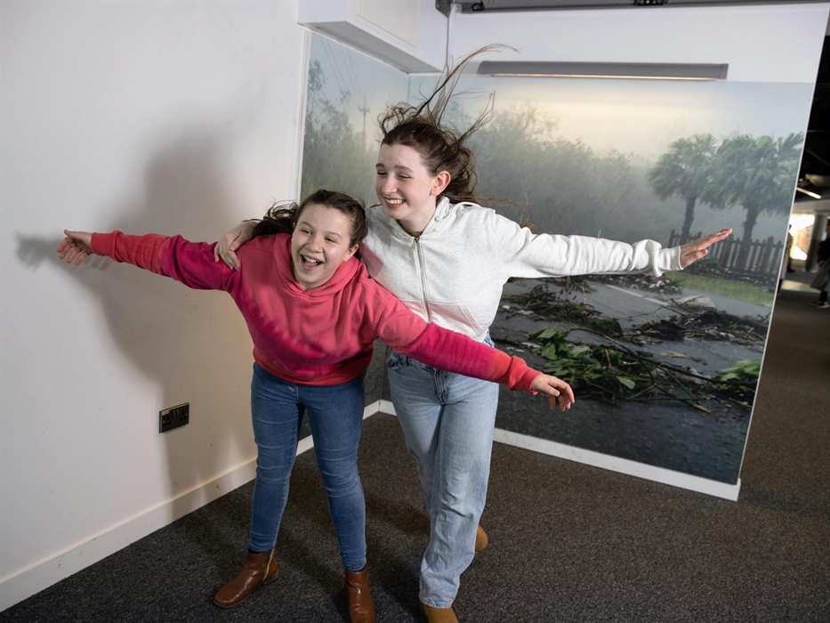 Two teenage visitors using the Hurricane exhibit, which uses a large fan to blow air at them at high speed.
