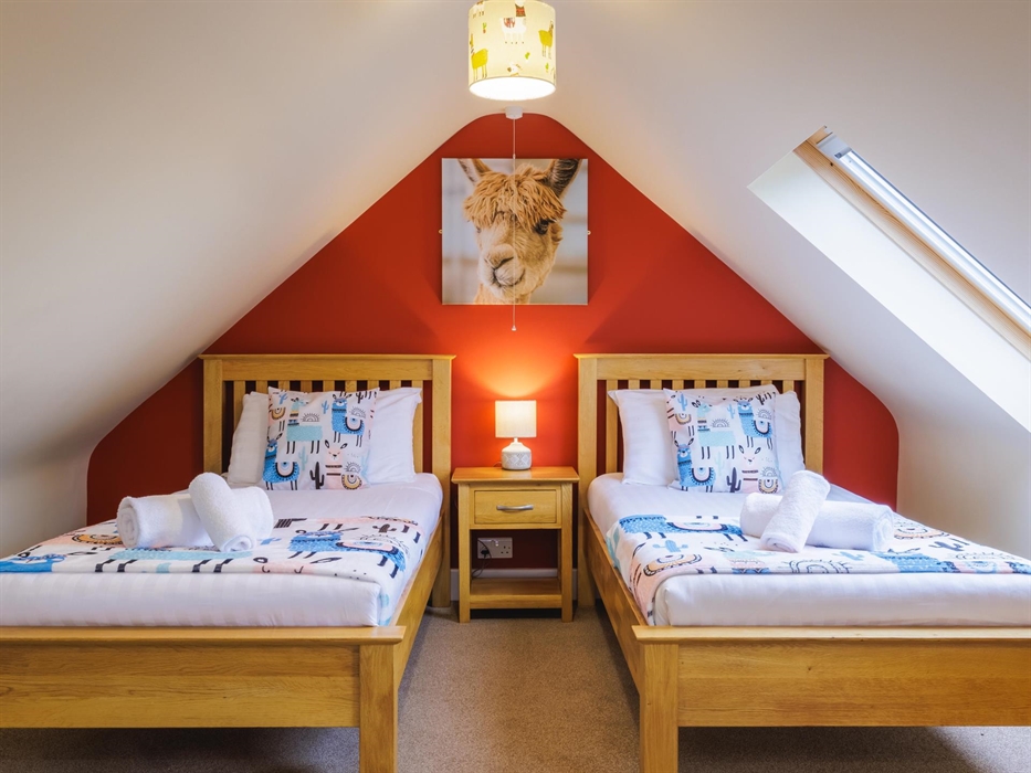 Large alpaca wall canvas above two full size single beds with side table and lamp and alpaca and Peruvian design accessories.