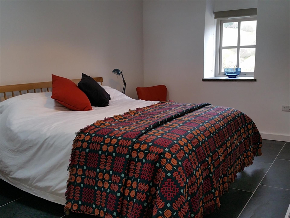 Super king sized bed with crisp white bed linen and a traditional Welsh blanket in warm dark colours of deep red, orange and teal.