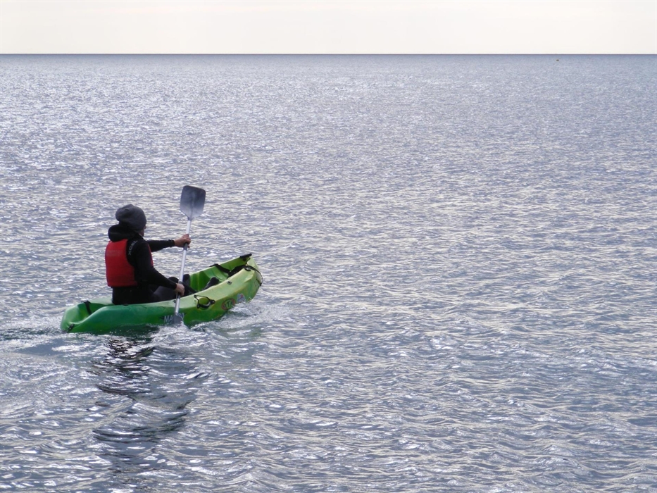 A single kayaker paddles accross a flat sea.