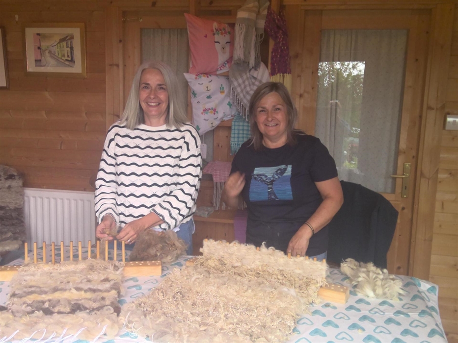 Two ladies enjoy a day weaving a seat pad on the peg loom in the log cabin.