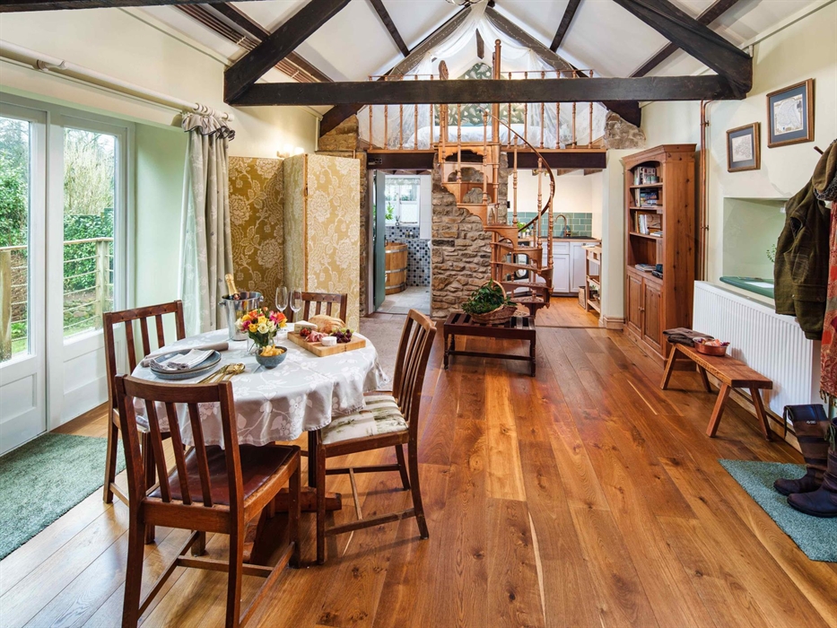 A view of inside the cottage. Dining table in the foreground and behind it is the kitchen and spiral staircase leading up to the bedroom.