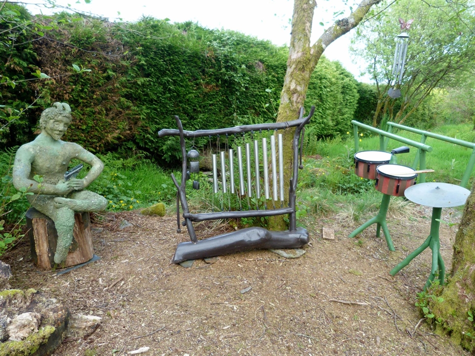 A statue of Pan  with a large xylophone, drums and cymbal. Bridge in the background over water