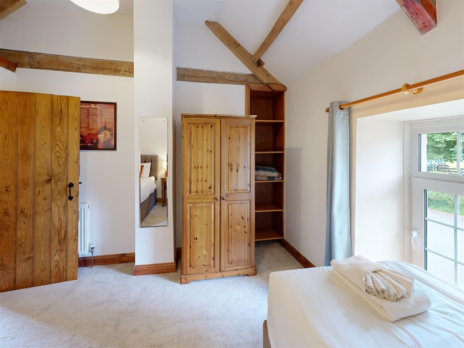 Twin bedroom with rustic wood wardrobe, ceiling beams, and garden views from two windows.