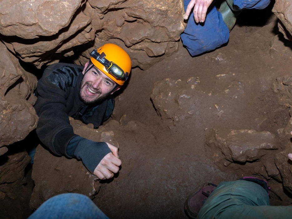 Smiling man wearing helmet climbing up through hole in cave