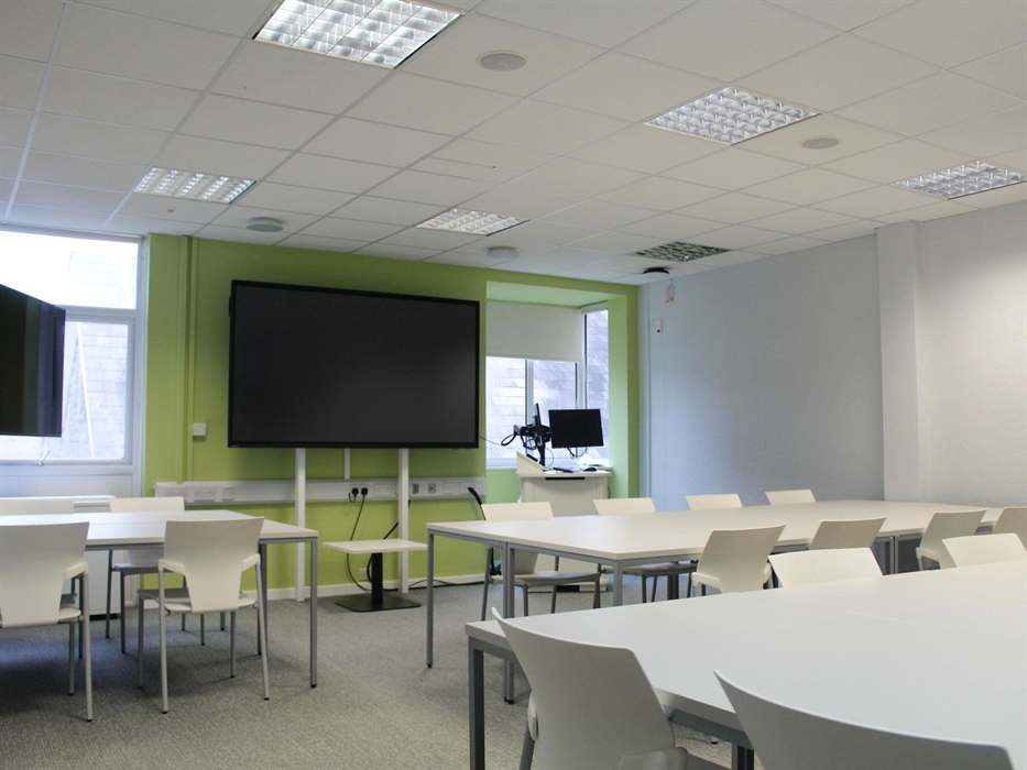 Classroom with tables, chairs and tv screen.