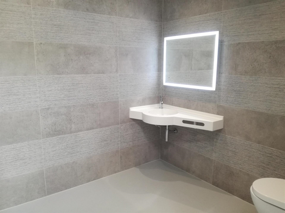 Contemporary bathroom with walk-in shower, grey tiled walls, and illuminated mirror.