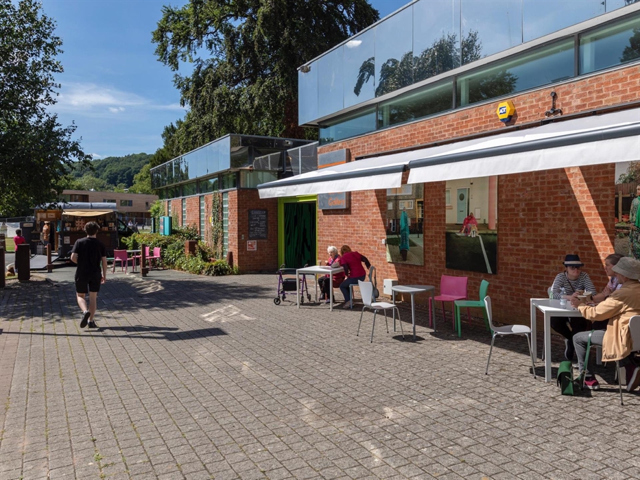 External angled view of gallery with awnings open and seating outside with visitors sitting underneath in the shade.