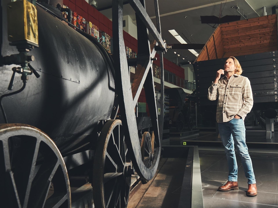 A man looks at a large black engine. It's a replica of Richard Trevithick's steam locomotive, the first steam powered vehicle to run on rails in 1804.