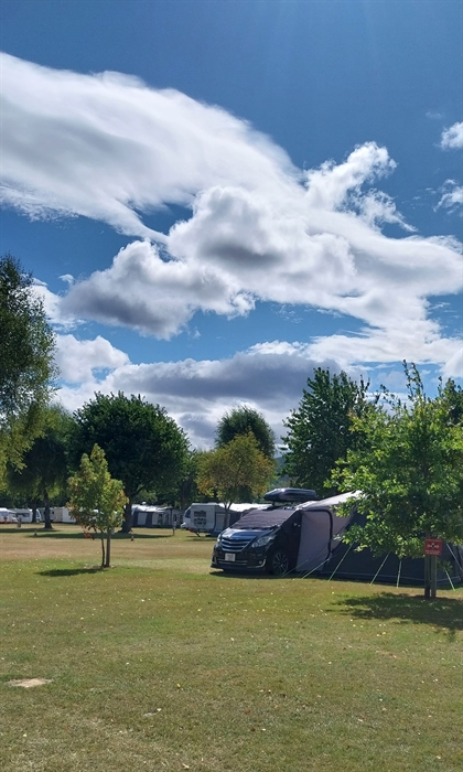 Campervan and awning set up by tree in main field of Pyscodlyn Caravan Park in summer