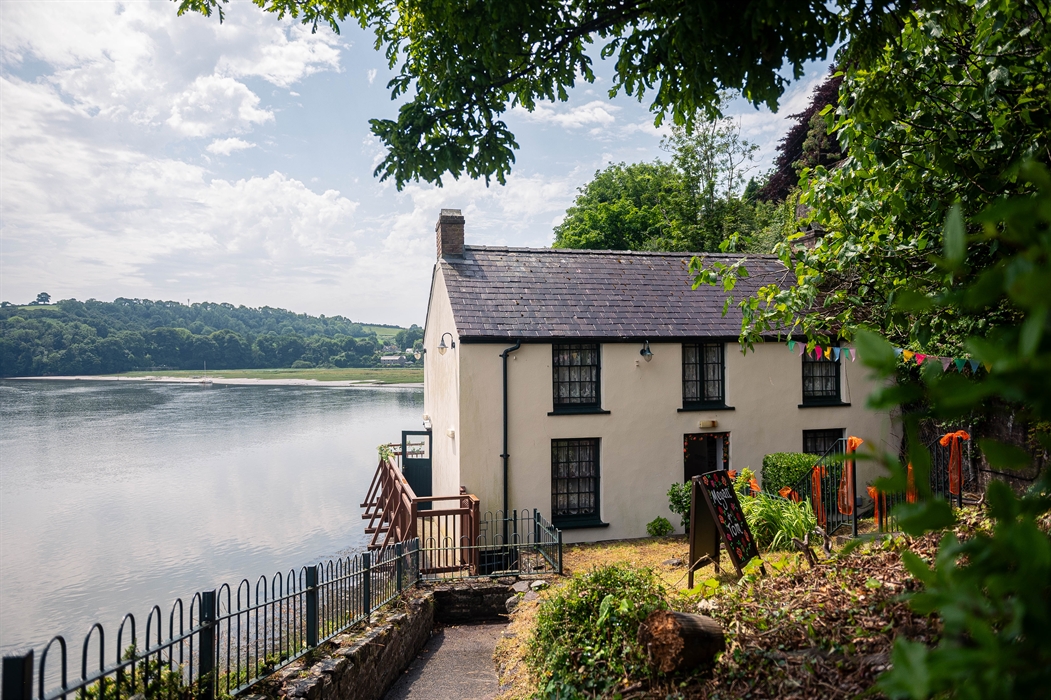 View of the front of the Boathouse from a pathway at the side of a small garden. The Taf estuary and Sir John's Hill can be seen in the distance behin