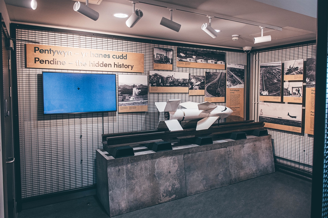 A small room with a white missile on a pedestal and rail in the centre. Metal walls display interpretation panels and photos.