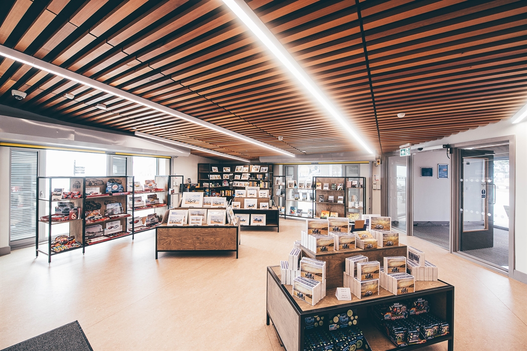A large, brightly lit gift shop. Two display tables are in the centre of the picture with shelving units behind.
