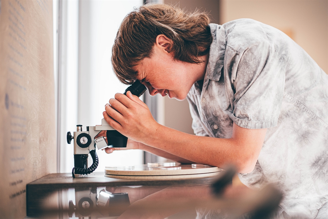 A teenage boy looks into a microscope