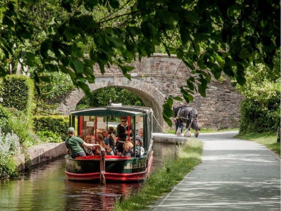 Scene of one of Llangollen Wharf's horse drawn boats travelling a long the Llangollen Canal heading to one of the historic stone bridges.
