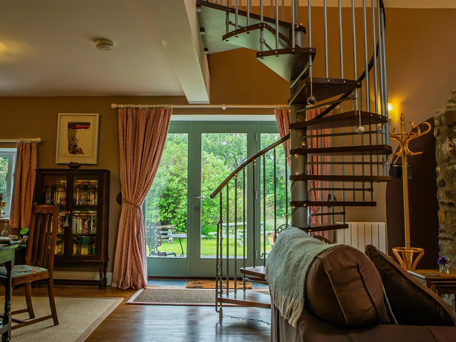 Hen Ffermdy cottage open plan living-dining area with spiral staircase to mezzanine bedroom and French window overlooking the gardens
