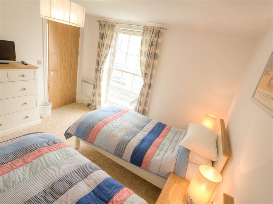Twin beds with bedside cabinet and lamps showing chest of drawers with TV and door to en-suite bathroom