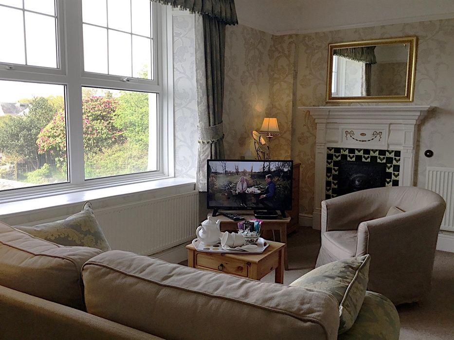 Double (king-size room) showing the sofa, TV and coffee table, with a large window overlooking the village and an original Edwardian tiled fireplace
