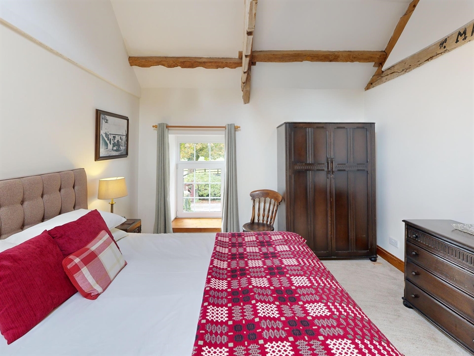 Another angle of the king bedroom at Ty Cerbyd showcasing exposed rafters, a skylight, and antique-style furniture, filled with natural light.