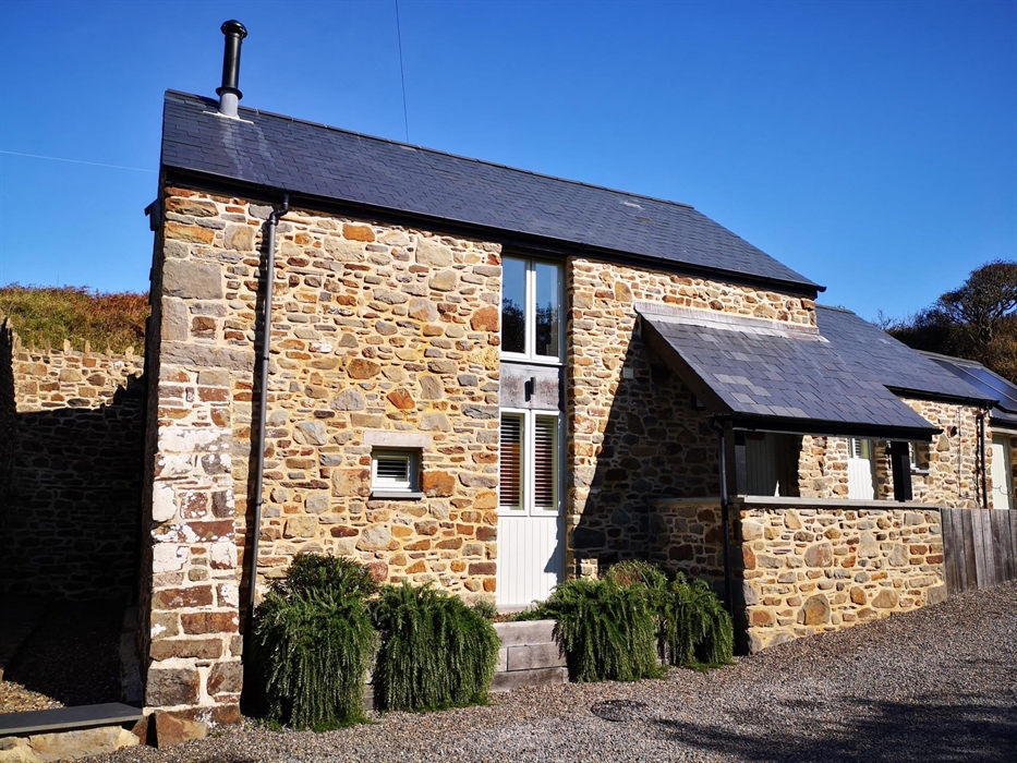 The Mill House seen from the drive on a blue sky day. Slate roof with stone walls.