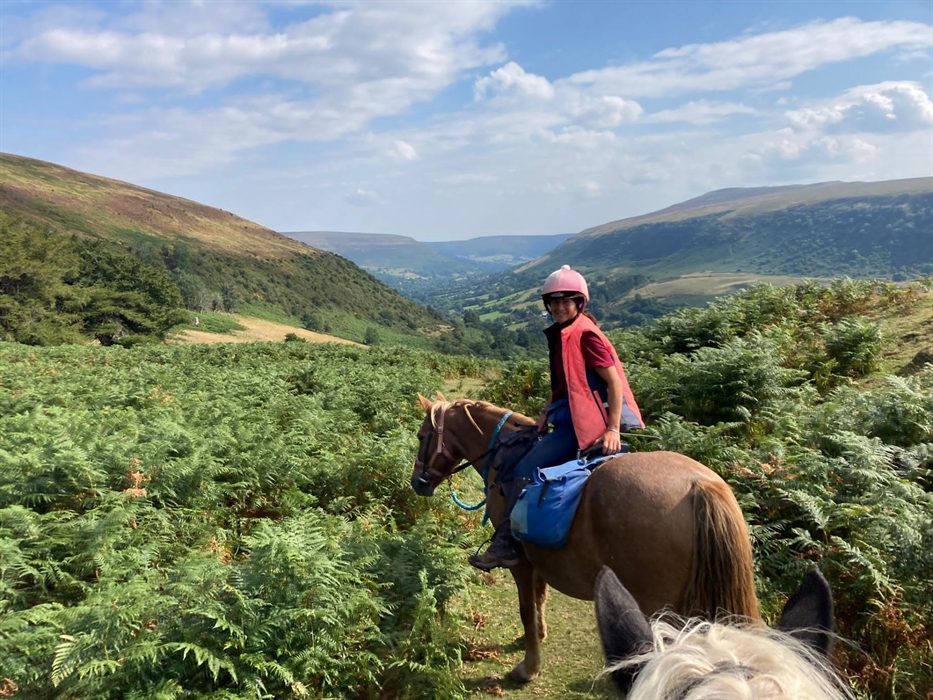 Trek leader Demelza turning around to chat to her customers on the way back from a full day trek with lunches in the blue saddle bag upon the horse.