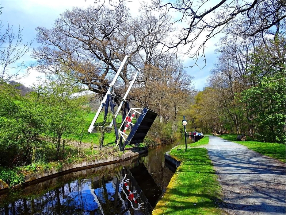 A scenic view of a Llangollen canal Lift Bridge edged by Trees, grassed edges and the Towpath.