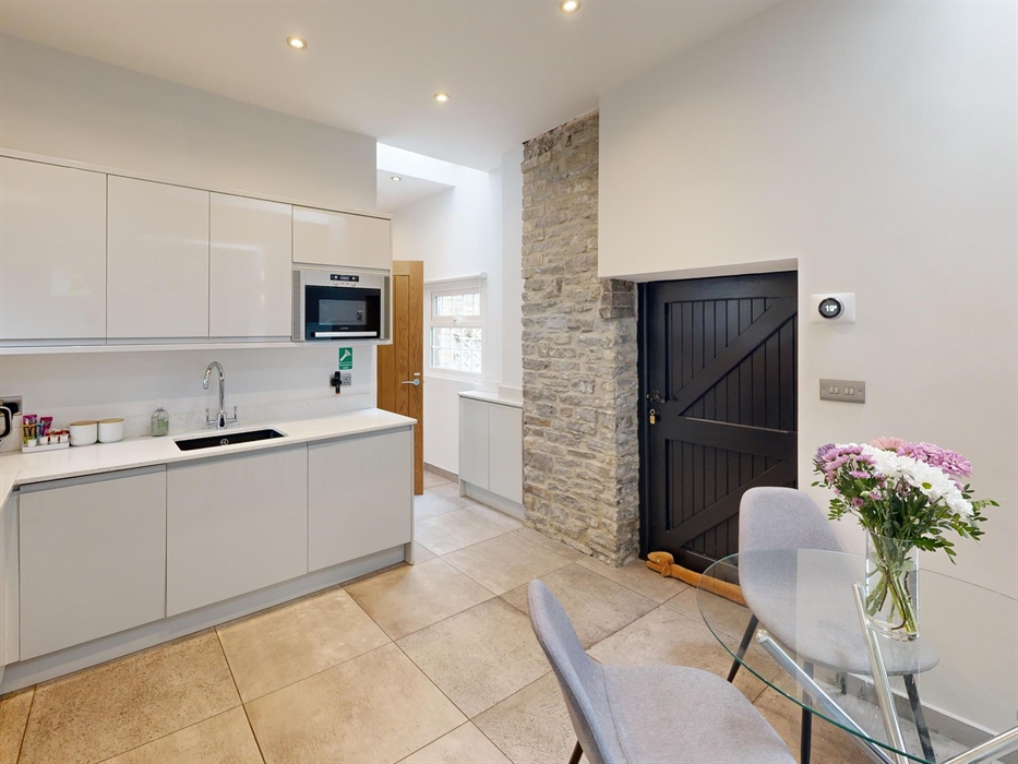 A bright and spacious kitchen with a glass dining table, exposed stonework, and a black stable door.
