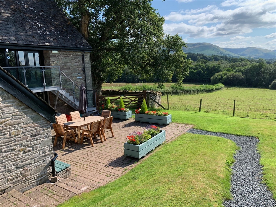 The Longhouse at Hilltops Brecon Holiday Cottages has a private outdoor patio area with views across open fields to the Camarthen Fans
