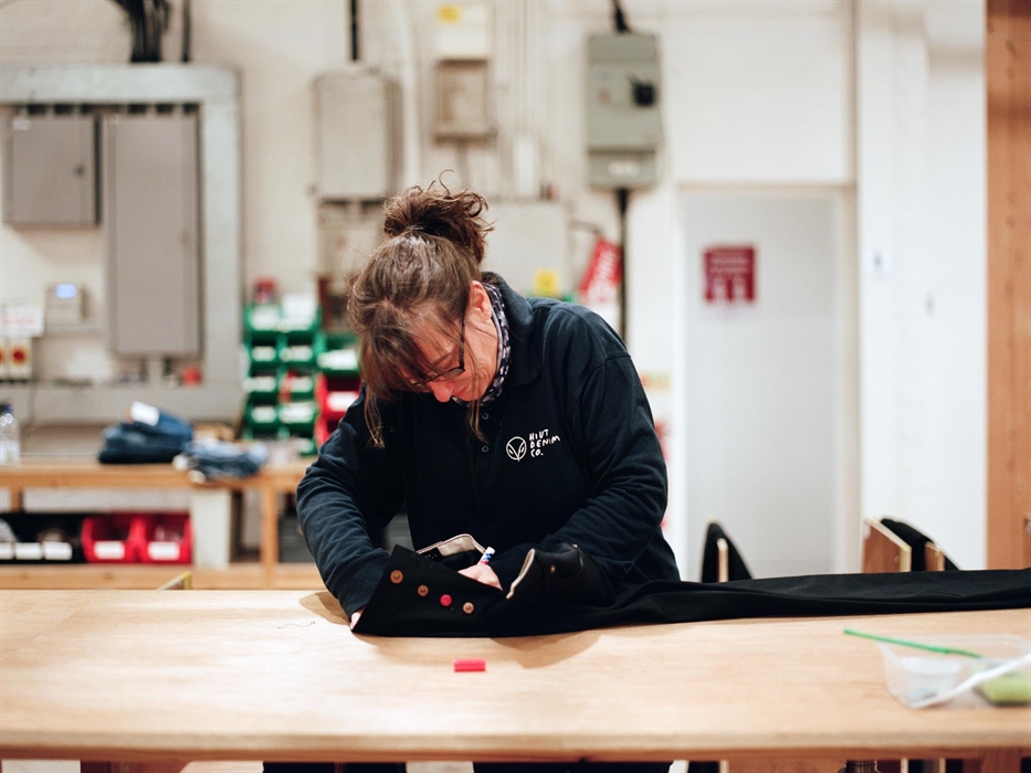 A Hiut Denim Grandmaster carefully signs a pair of finished jeans on a large wooden worktable. She’s focused on the details, reflecting the brand’s de