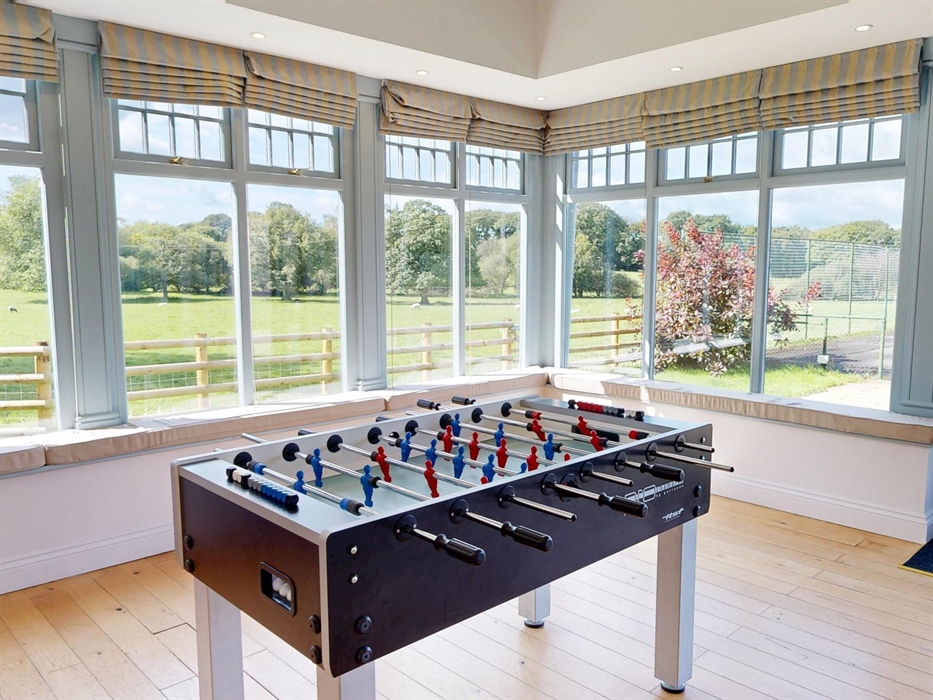 Foosball table in a bright games room with large windows offering sweeping views of fields, trees, and open sky.