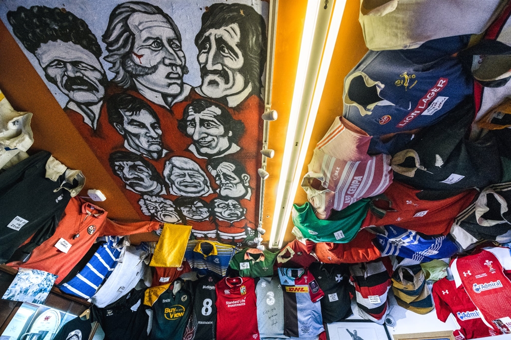 The photo shows a variety of different rugby jerseys attached the ceiling and a painting of Welsh rugby stars.
