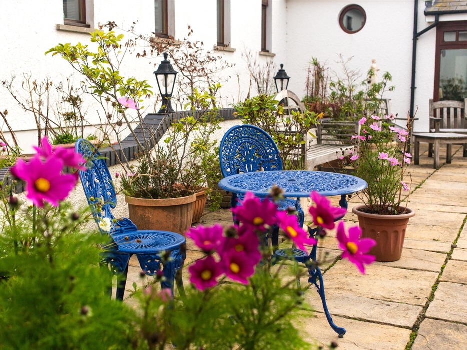 Ael y Bryn courtyard; benches and tables with summer flowers and potted plants.