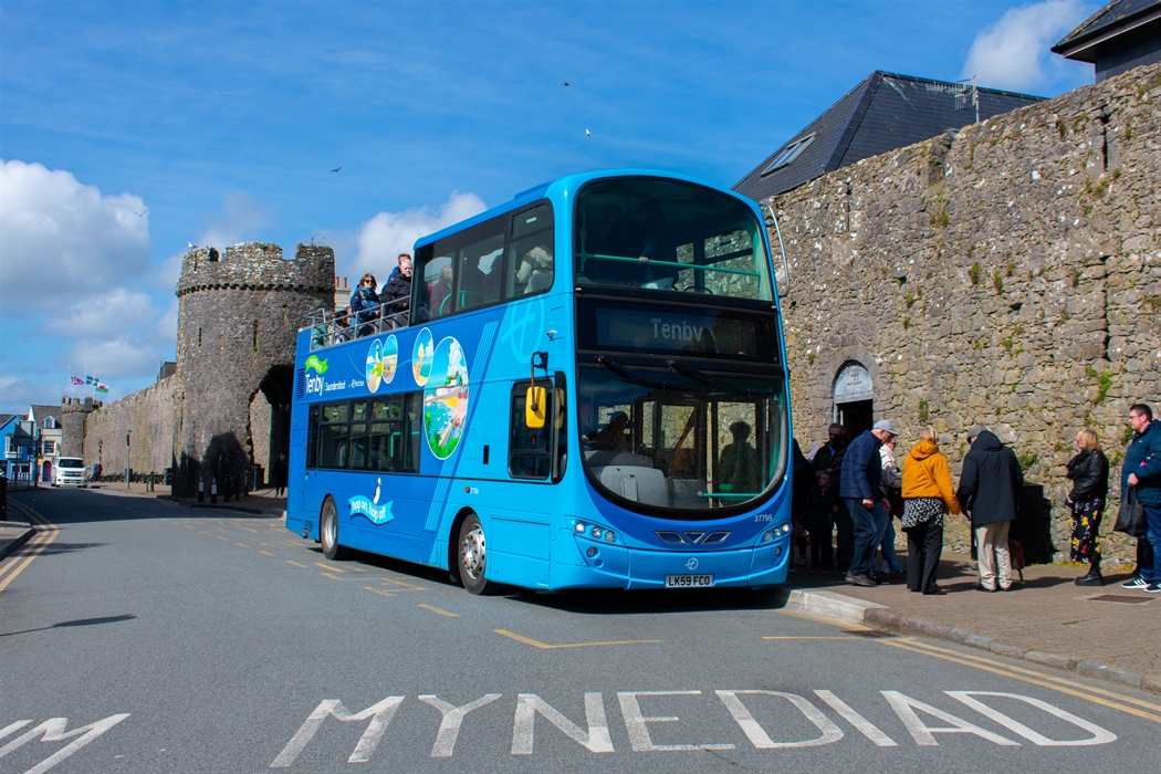 an open-top bus dropping off passengers at a bus stop