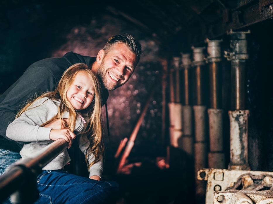 a father and young daughter look along a line of modern pit props, steel bars used to hold up the roof in a coal mine. They are in the King Coal exper