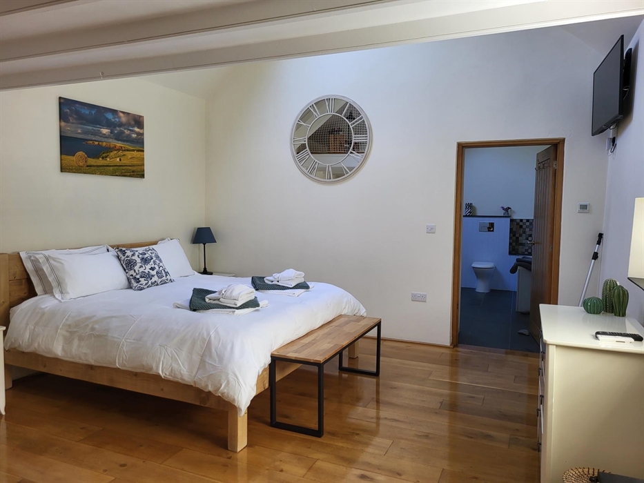 Barn room ready for guests: Super king bed with towels folded at the foot. Wooden floor, solid chunky wooden bed, with a picture of the local countrys
