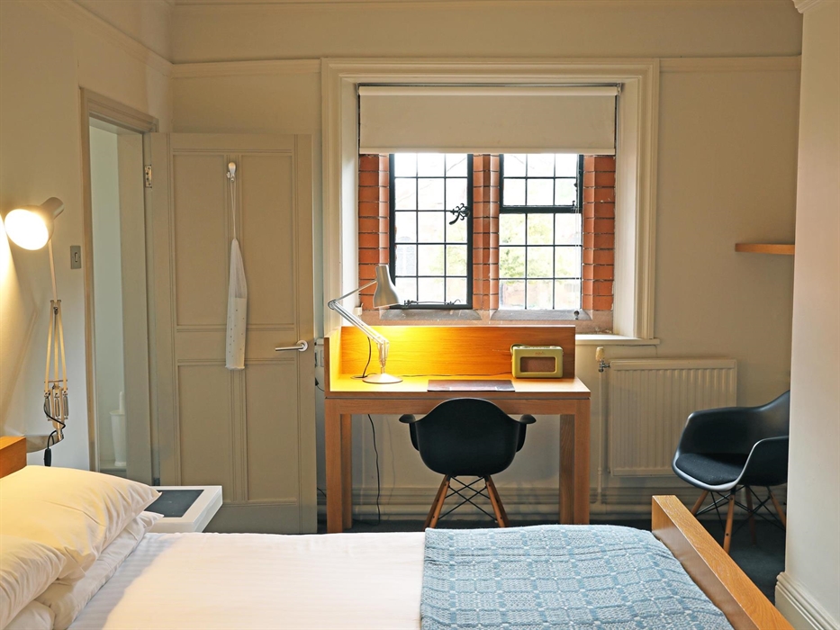 A view over a single bed showing a desk and chair before a window and the entrance to a bathroom on the right