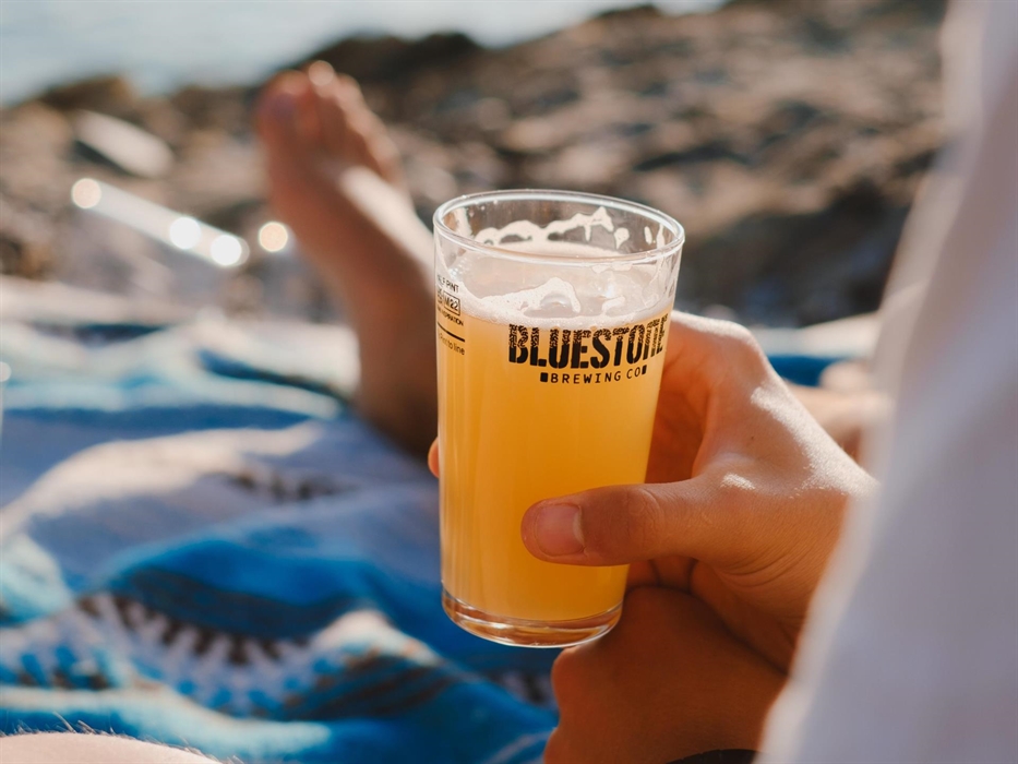 A hand is holding a half pint glass of beer, the sun is shining